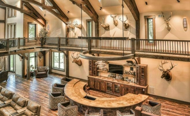 Interior of a Custom Timber Frame Residence in WI with dark stained, arched king post trusses, cathedral windows and ceilings, and a stone fireplace.