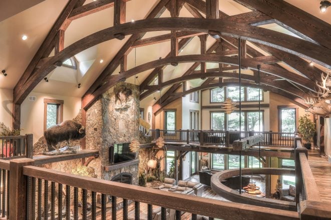 Interior of a Custom Timber Frame Residence in WI with dark stained, arched king post trusses, cathedral windows and ceilings, and a stone fireplace.