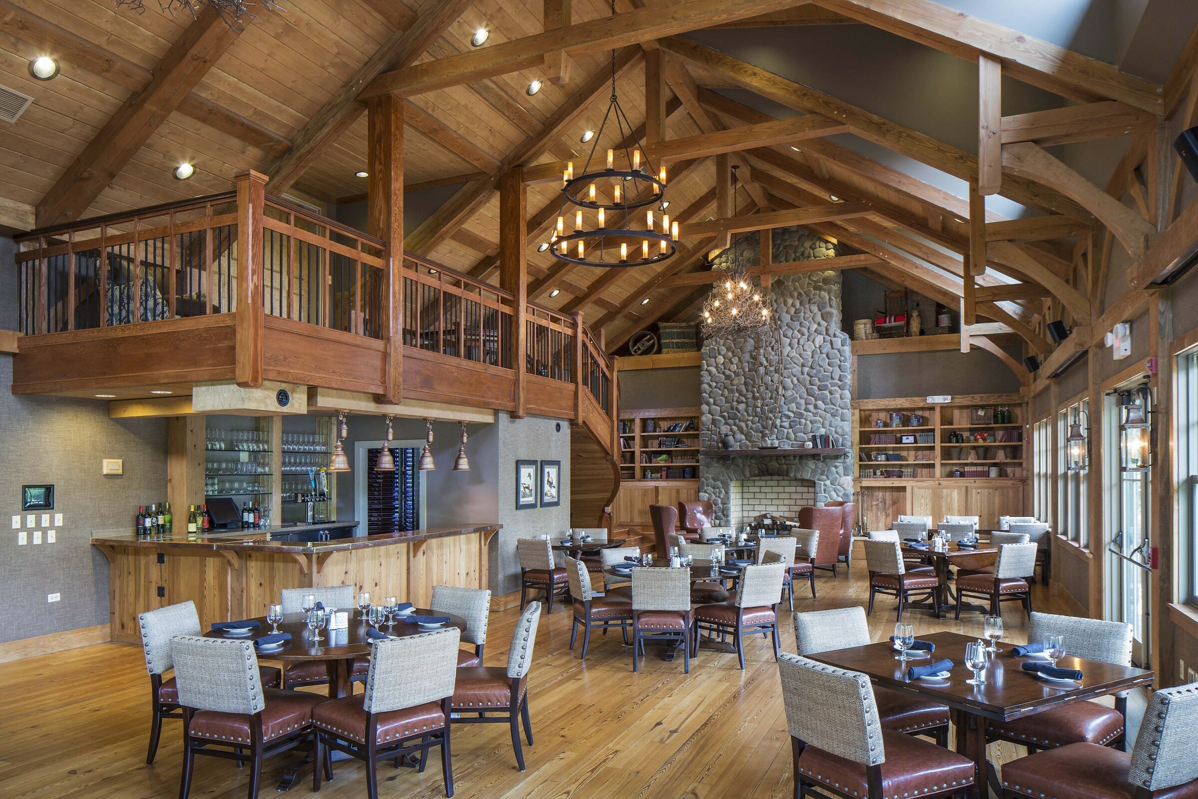 Interior of the South River Golf Club dining room and event space that features Timber Trusses, a Cathedral ceiling, and a tall stone fireplace.