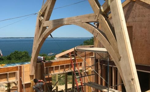 The reclaimed oak hammer beam truss being lowered into place by crane at the Seven Gates Residence in Martha's Vineyard