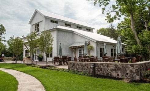 Exterior of the Briar Barn Inn in Rowley, MA. Built by Vermont Timber Works in the Monitor Barn Style. There is outdoor seating on the stone patio outside the barn.