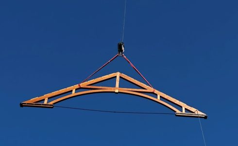 Arched Timber Truss being flown into place by a crane.