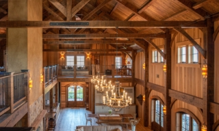 Rustic timber banquet hall with exposed beams, chandeliers, and arched windows.