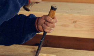 Child's hands hammering a nail into a wooden beam with a hammer in hand